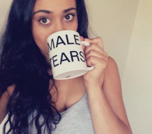 A young woman drinking from a cup that is labeled "male tears."