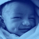 close-up of infant baby wrapped in a blanket and smiling, blue filter.