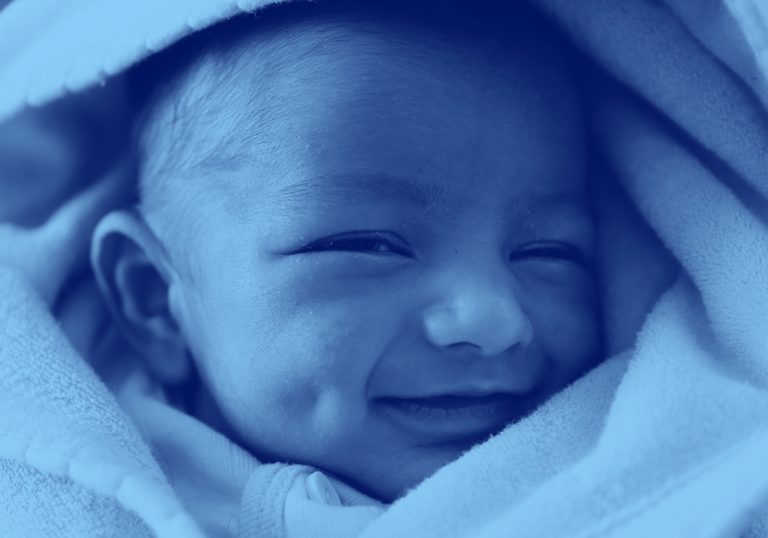 close-up of infant baby wrapped in a blanket and smiling, blue filter.