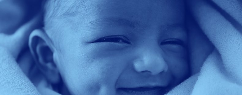 close-up of infant baby wrapped in a blanket and smiling, blue filter.