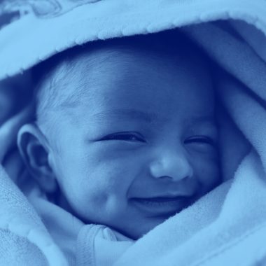close-up of infant baby wrapped in a blanket and smiling, blue filter.