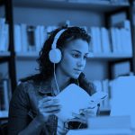 young woman wearing headphones with a book in hand studying, blue filter.
