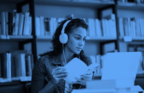 young woman wearing headphones with a book in hand studying, blue filter.