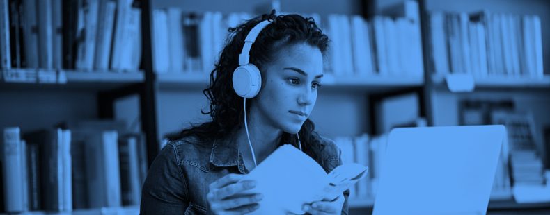 young woman wearing headphones with a book in hand studying, blue filter.