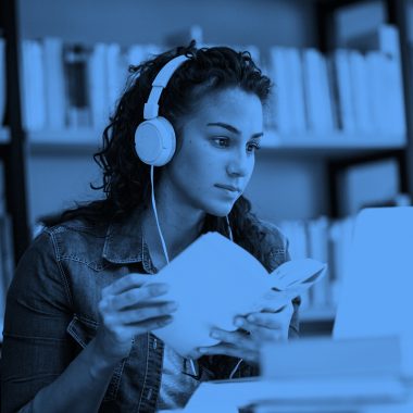 young woman wearing headphones with a book in hand studying, blue filter.