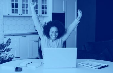 girl raising hands triumphantly while sitting at table with computer