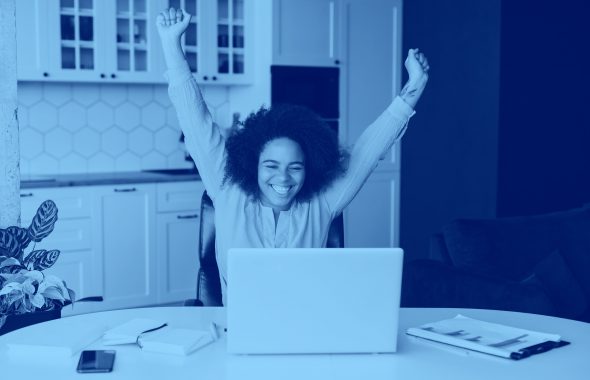 girl raising hands triumphantly while sitting at table with computer