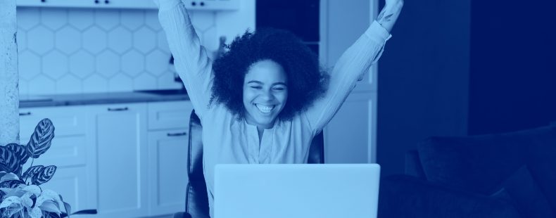 girl raising hands triumphantly while sitting at table with computer