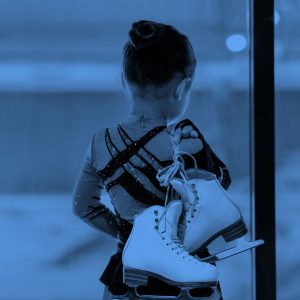 Back view portrait of little girl holding figure skates standing by indoor ice rink and watching workout
