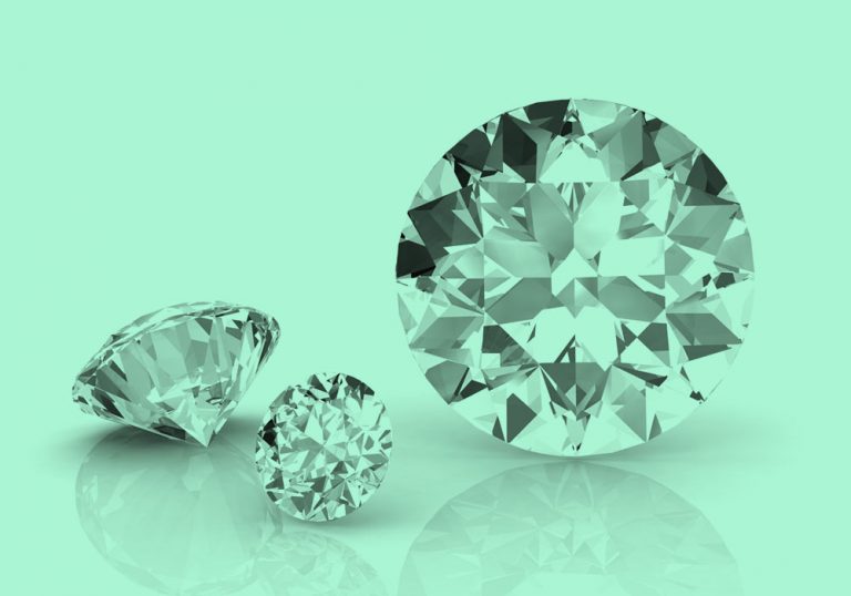 3 diamonds of different sizes, their reflections visible on the tabletop, teal filter.
