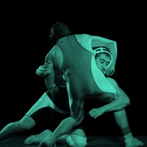 two young male wrestling athletes gripping each other in wrestling holds, in a teal filter.