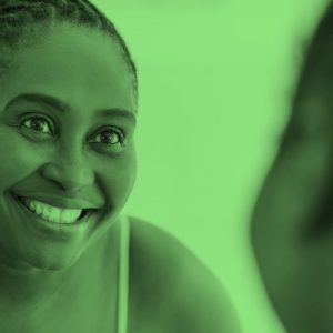 young Black woman smiling in the mirror, green filter.