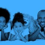 family of three (mom, daughter, and dad) lying on their bellies and smiling at the camera, blue filter.
