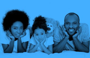 family of three (mom, daughter, and dad) lying on their bellies and smiling at the camera, blue filter.