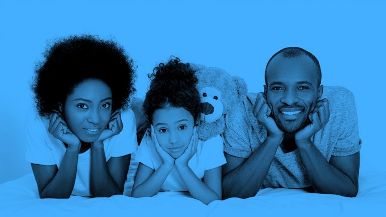 family of three (mom, daughter, and dad) lying on their bellies and smiling at the camera, blue filter.