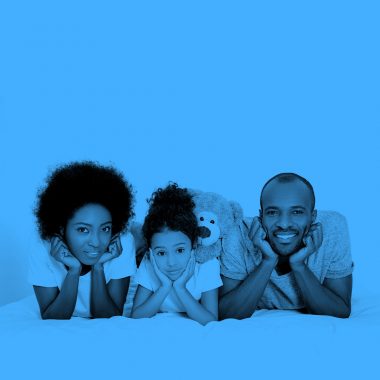 family of three (mom, daughter, and dad) lying on their bellies and smiling at the camera, blue filter.