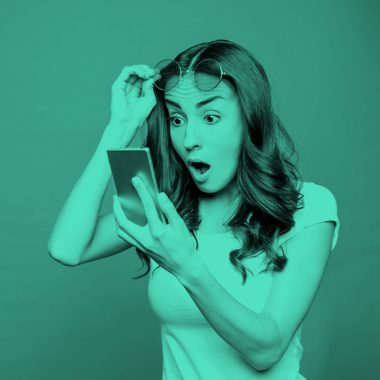 image of shocked woman looking at her phone, teal filter.