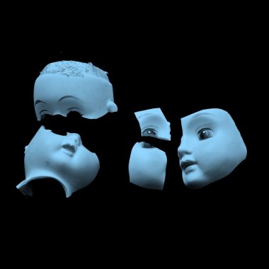 blue filtered image of broken pieces of porcelain doll's head, on black background.