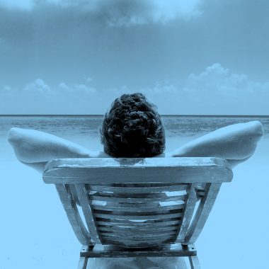 rear view of man reclining on a beach chair in front of ocean, blue filter.