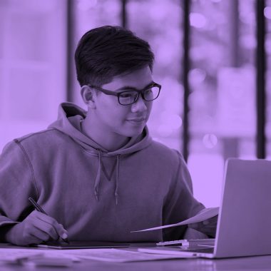 male student working on laptop, purple filter
